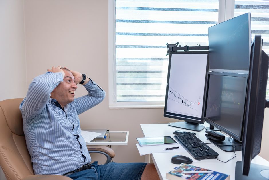 Calculate trading position size — A thrilled man reacts to financial market trends on multiple monitors in a modern office