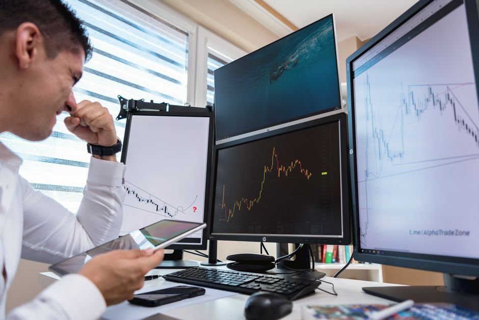 Scalping vs day trading — Trader in white shirt analyzing stock charts on multiple monitors during daytime in an office