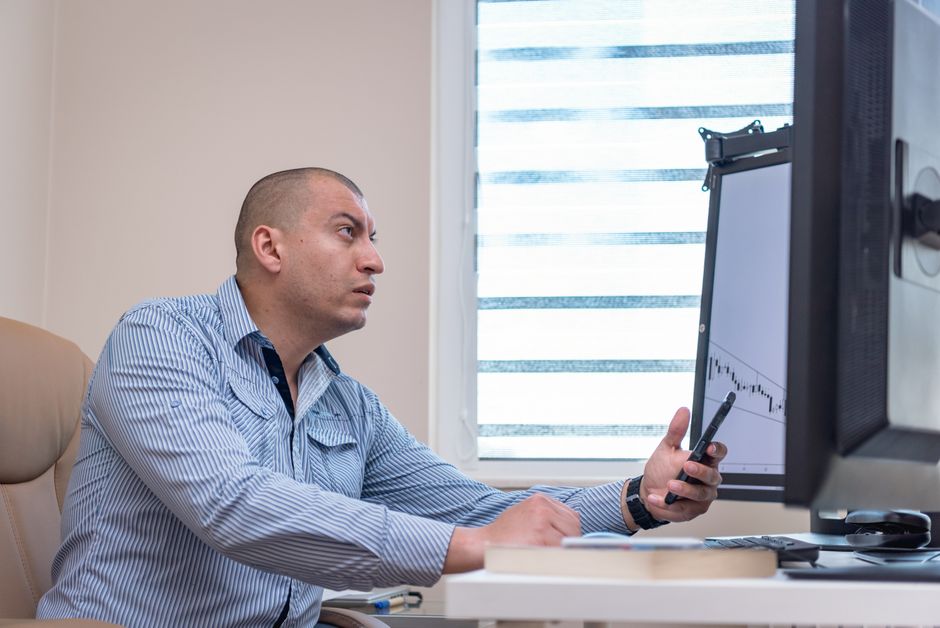 Scalping vs day trading — A man intensely studies financial graphs on a computer with a smartphone in hand, working in an